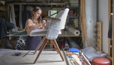 Een vrouw stoffeert een stoeltje dat op een tafel staat