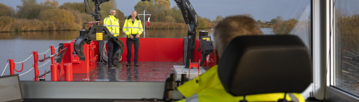 Frans Stafleu zit in de stuurhut van het gloednieuwe elektrische werkschip Eem Surveyor. Hij kijkt voor zich. Twee collega's staan op het dek.