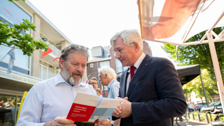 Wethouder Pim van de Veerdonk en gedeputeerde André van Schie in gesprek over fietsstimulering aan de hand van een folder.