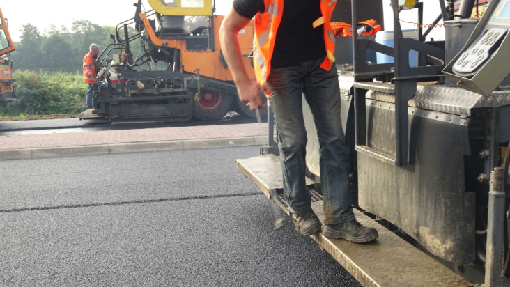 Met een asfaltmachine wordt nieuw asfalt aangebracht op een provinciale weg.