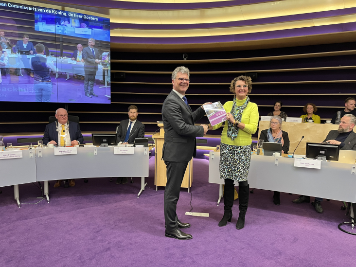 Een raadslid van de gemeente Nieuwegein overhandigt de profielschets voor de nieuwe burgemeester aan commissaris van de koning Hans Oosters