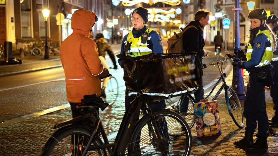 Politieagent spreekt met staande gehouden fietsbezorger in feloranje jas