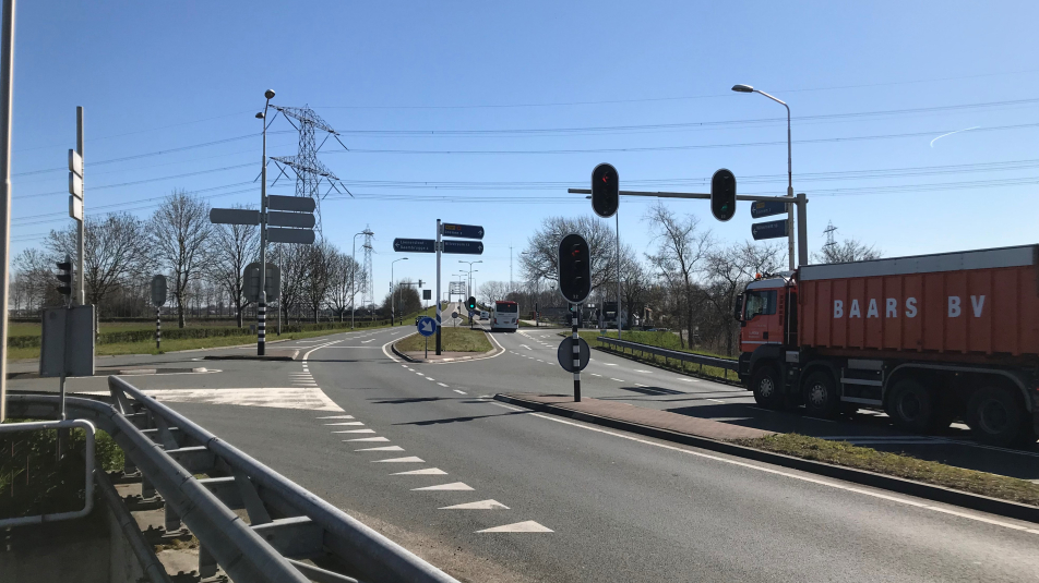 Op de afbeelding is het kruispunt in de N201 bij Loenersloot te zien met verkeerslichten, een vrachtauto en in de verte een brug.