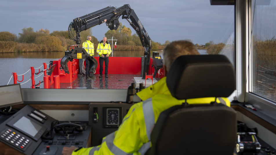 Frans Stafleu zit in de stuurhut van het gloednieuwe elektrische werkschip Eem Surveyor. Hij kijkt voor zich. Twee collega's staan op het dek.