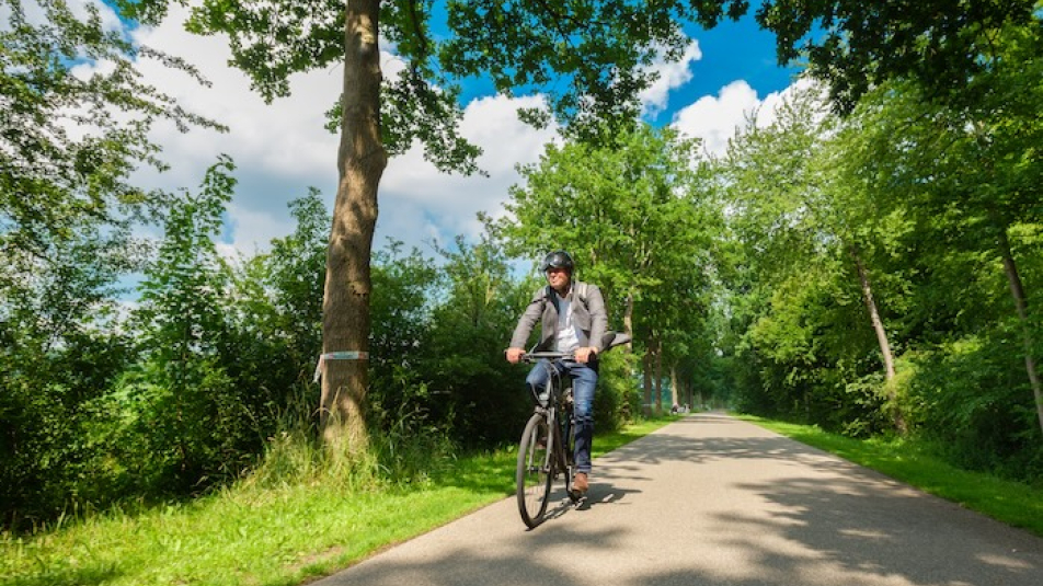 Man met fiethelm fietst in een groene omgeving